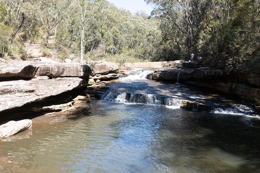Water flowing over The Weir sandstone wall into a calm swimming pool in Dharawal National Park