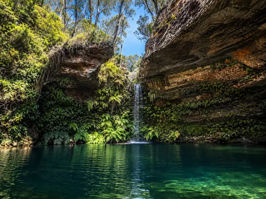 Waterfall falling into the emerald Pool of Diana beneath a sandstone overhang, with a small sandy beach on the Newnes Plateau