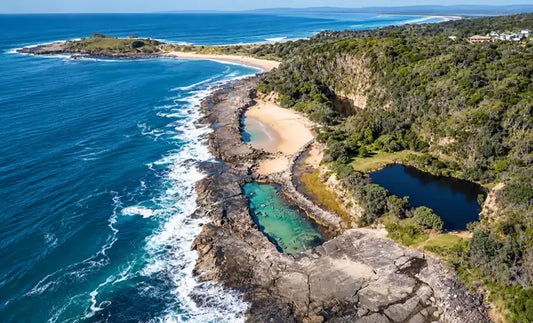 Deep emerald water of the Angourie Blue Pool surrounded by rock walls and grassy banks beside the ocean near Yamba