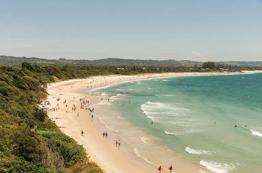 Golden sand and rolling surf along Tallow Beach, with Cape Byron's forested headland rising at the northern end