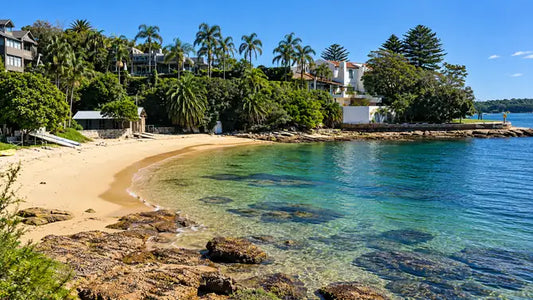 Narrow strip of sand at Kutti Beach, Vaucluse, lined with heritage timber boathouses on calm harbour water