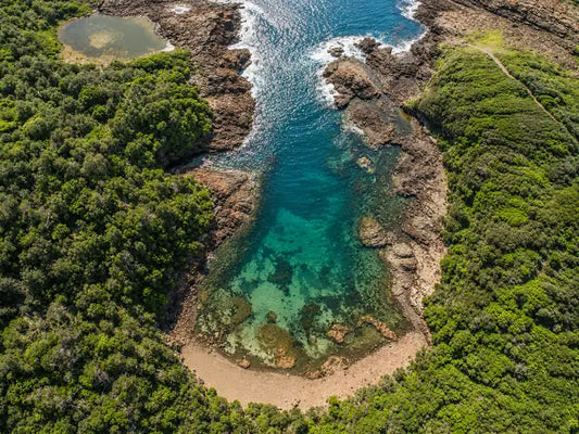 Clear blue water of Bushrangers Bay surrounded by dark basalt cliffs and coastal scrub at Bass Point
