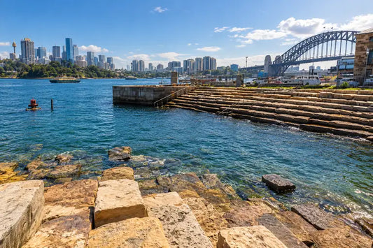 Swimmers at Marrinawi Cove, Barangaroo, with tiered sandstone blocks stepping into Sydney Harbour and city towers behind