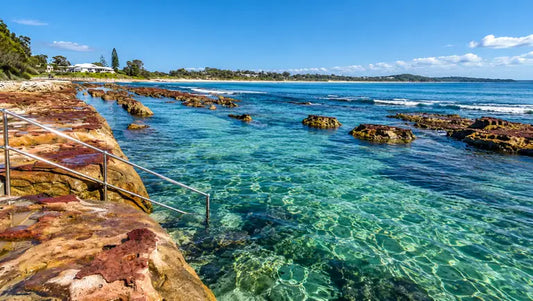Clear, shallow water of Currarong Rockpool with a sandy floor, low wall and rocky shoreline