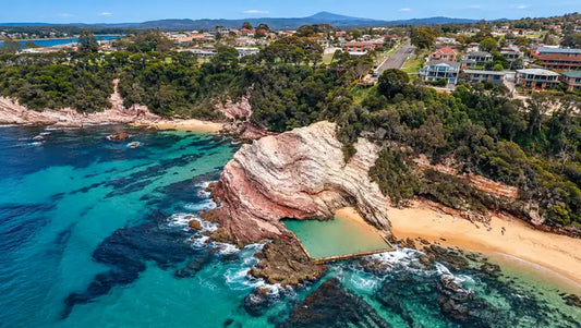 Aslings Beach rock pool in Eden set into reddish rock below the cliffs, with clear water and the ocean beyond